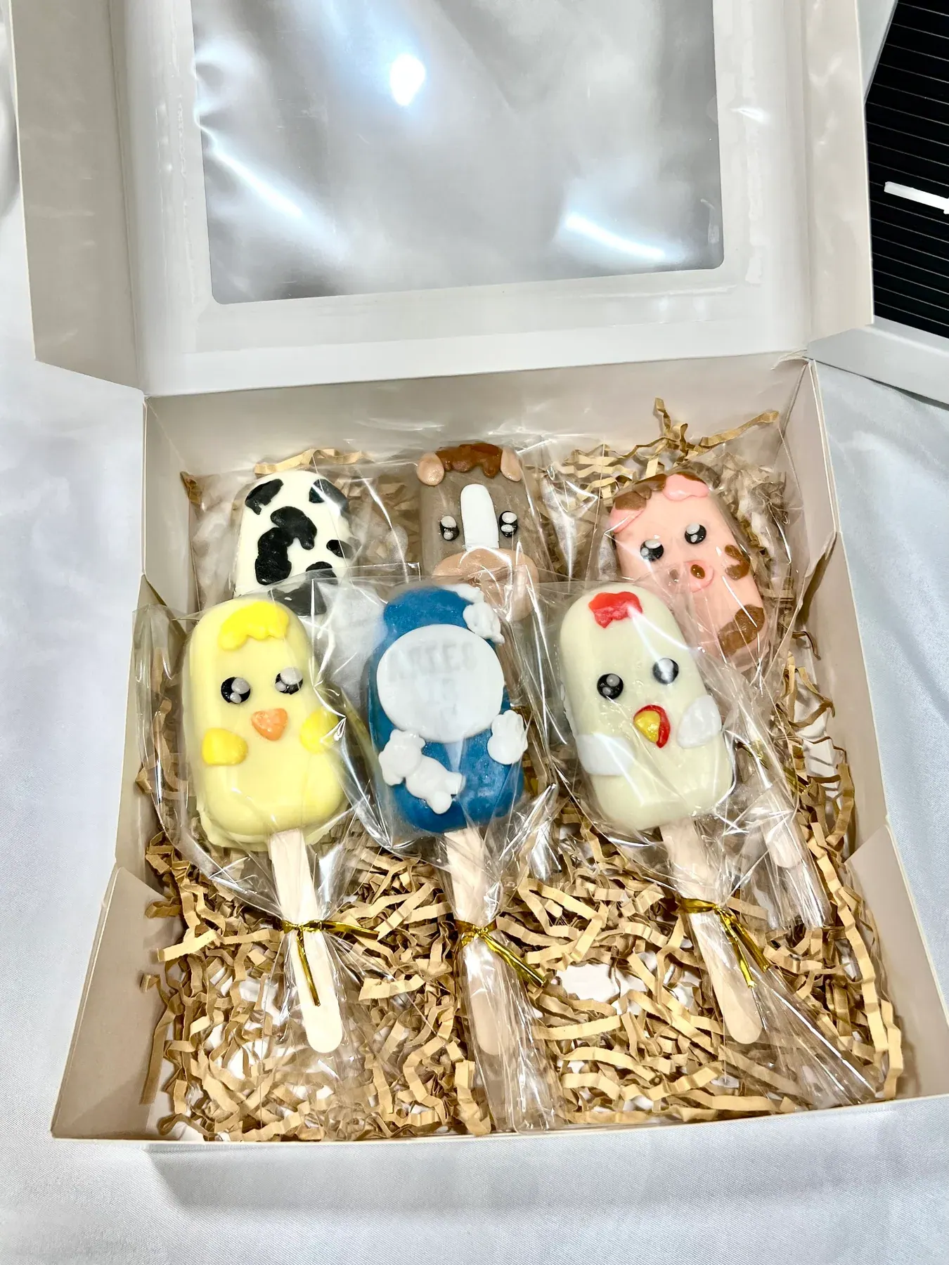 A box of animal cakesicles: a cow, a chick, a pig and more, each wrapped