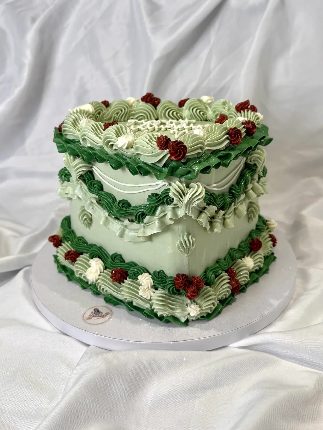 Vintage heart-shaped cake in sage green with layered piped shells, frills and red cherries