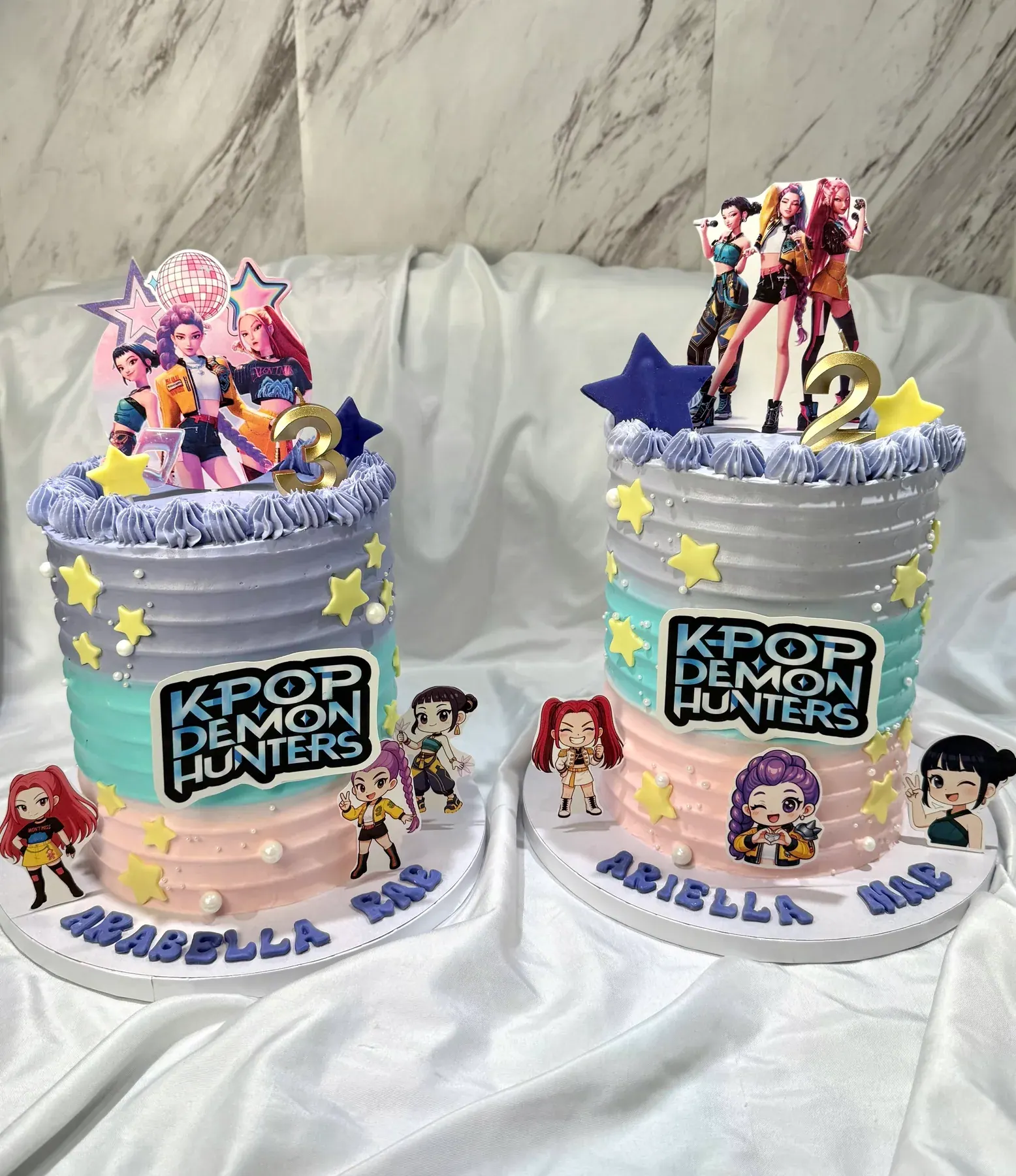 A matching pair of K-pop Demon Hunters birthday cakes with character toppers, stars and piped stripes