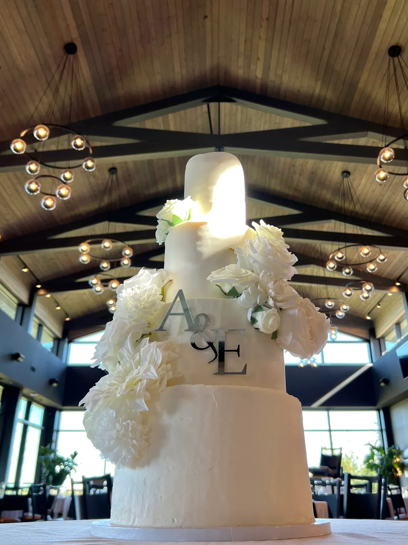 Tall four-tier white wedding cake with cascading white flowers in a vaulted hall