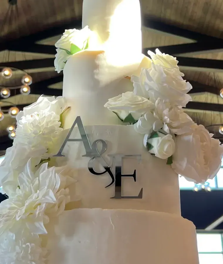 Close-up of a silver A and E monogram among white sugar flowers on a tall wedding cake
