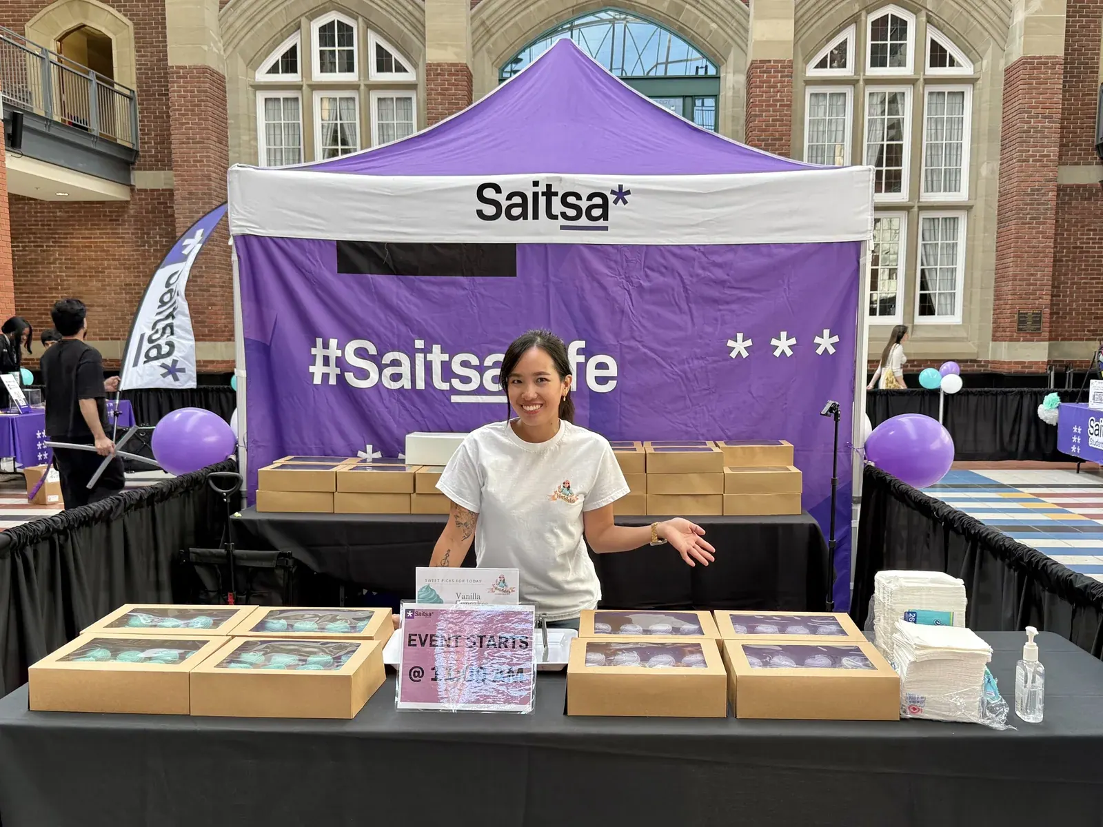 Nicole smiling behind her Nicsdelite table of boxed cupcakes at a SAITSA campus event